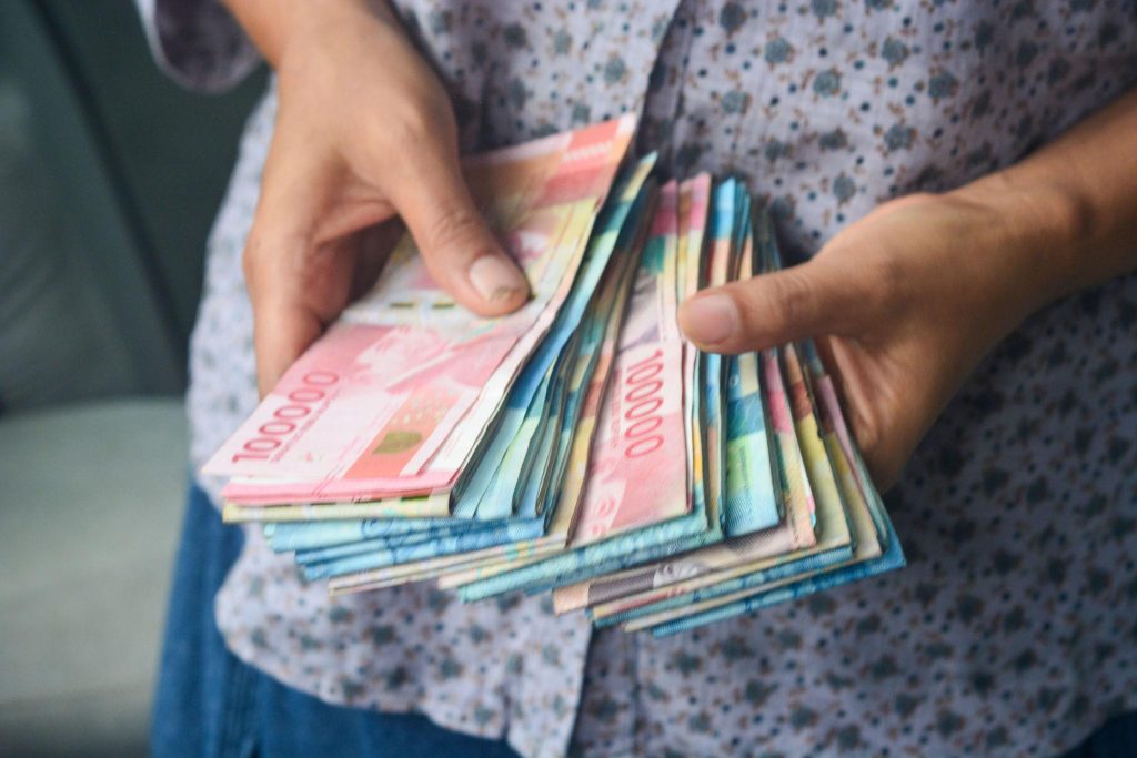 Seseorang memegang dan menghitung tumpukan uang rupiah.