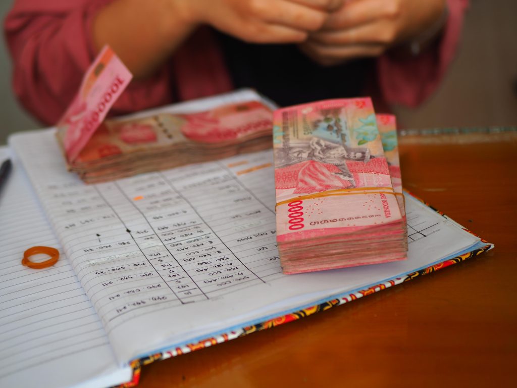 Tumpukan uang rupiah di atas buku catatan keuangan yang menunjukkan pengelolaan biaya operasional dalam bisnis supplier.