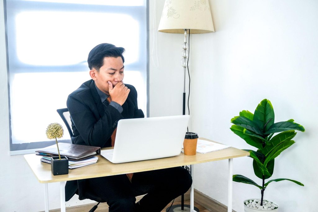 Seorang pria duduk di depan laptop terlihat berpikir serius di meja kerja.